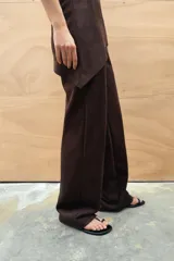 Pantalón de tiro alto color marrón, confeccionado en tejido efecto ante. Presenta trabillas, falsos bolsillos de vivo en el delantero y cierre frontal con cremallera y gancho metálico.