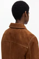 Chaqueta corta marrón de acabado cepillado suave con costuras en contraste. Cuenta con cuello clásico, cierre frontal de botones, bolsillos de parche delanteros y mangas largas.