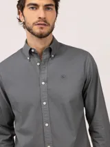 Camisa de hombre de corte regular fit, color gris oscuro, confeccionada en algodón con acabado vintage de tintado en prenda. Cuenta con cuello button-down, cierre frontal de botones, manga larga y logo bordado en el pecho.