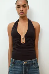 Body de cuello halter con espalda descubierta, confeccionado en poliamida. Presenta un diseño drapeado en los laterales y una abertura frontal con detalle metálico. Posee cierre con botones a presión en la parte inferior y lazada en el cuello.