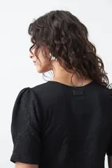 Remera negra de manga corta con textura floral en relieve. Presenta un diseño de inspiración romántica con mangas ligeramente abullonadas que aportan estructura y un ajuste al cuerpo.