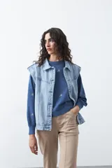 Chaleco de jean en tono celeste claro, con corte recto, cuello camisero, cierre frontal con botones metálicos y costuras visibles.