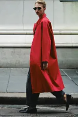 Trench largo ZARA Woman Collection de color rojo con cuello solapa, manga larga y bolsillos laterales ocultos. Presenta forro interior a contraste y cierre frontal con botones a presión.