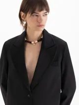 Saco sastrero estructurado de color negro, con largo hasta la rodilla, cuello con solapa de pico ancha y cierre frontal de dos botones. Cuenta con bolsillos con solapa y está completamente forrado.