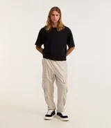 Pantalón cargo recto color beige, con cintura elástica ajustable con cordón, bolsillos laterales tipo cargo con solapa y bolsillos con cremallera.