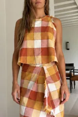 Top de calce suelto con diseño a cuadros en tonos mostaza, naranja y blanco. Es liviano y fresco, con detalles desflecados en los bordes.