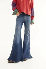 Jean de corte oxford y tiro medio, confeccionado en denim azul con lavado localizado. Presenta recortes curvos en la parte superior y aberturas laterales en la botamanga decoradas con botones metálicos y terminación desflecada.