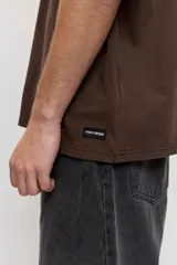 Remera marrón oversize de manga corta, con cuello redondo y pequeños estampados blancos en el pecho.