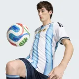 Camiseta de fútbol Adidas de la Selección Argentina, modelo titular 2026, versión jugador. Diseño a rayas verticales celestes y blancas, con cuello redondo y detalles en azul marino en las mangas y hombros. Incluye escudo de la AFA y logo de Adidas en dorado, además del parche de campeón FIFA.