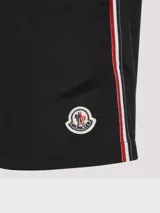 Short de baño negro con cintura elástica y cordón ajustable. Presenta una franja tricolor (rojo, blanco y azul) en los laterales y el logo de Moncler en el bajo.
