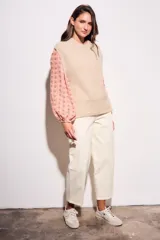 Chaleco de punto color beige con cuello alto y sisas amplias.