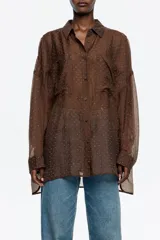 Camisa oversize de tejido fantasía marrón oscuro, con minipiedras distribuidas por toda la prenda. Presenta cuello camisero, botones frontales, bolsillos de plastrón en el pecho y mangas largas con puño abotonado.