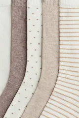 Pack de siete pares de medias tobilleras de punto fino, en tonos neutros como blanco roto, beige, y marrón topo. Los diseños incluyen rayas finas, lunares pequeños y texturas lisas.