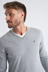 Sweater de tejido de punto color beige, con escote en V, mangas largas y puños y dobladillo acanalados. Presenta un pequeño logo bordado en el pecho.