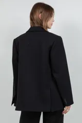 Blazer oversize negro con un sutil brillo, solapas de muesca, doble botonadura frontal y bolsillos con solapa.