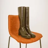 Botas altas de cuero color negro con diseño texturizado estilo animal print tipo cocodrilo en la parte frontal y trasera, taco cuadrado y puntera cuadrada.