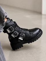 Bota tipo borcego de cuero color marrón oscuro, con suela track negra y tres correas horizontales con hebillas metálicas plateadas.