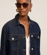 Campera trucker de jeans azul oscuro, corte amplio, con cuello clásico, cierre frontal con botones blancos, mangas largas y bolsillos delanteros con solapa.