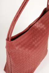 Bolso tipo shopper de símil cuero trenzado color marrón oscuro, con asas fijas centrales y gran compartimiento interior con tres bolsillos adicionales.