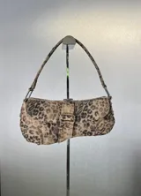 Cartera tipo baguette con estampado animal print en tonos marrones y beige. Tiene correa corta para llevar al hombro, cierre con solapa y hebilla decorativa.