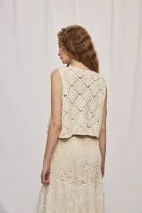 Chaleco corto de algodón color beige, confeccionado con un diseño calado en rombos, escote en V y cierre frontal con lazo para anudar.