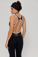 Mono deportivo de una pieza en color negro, con diseño de corte ajustado en el torso y piernas ligeramente acampanadas. Presenta detalles de líneas blancas contrastantes a lo largo de los laterales y en el escote, con espalda estilo nadadora.
