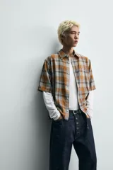Camisa de corte boxy fit confeccionada en tejido de algodón, con estampado de cuadros en tonos tierra. Presenta cuello solapa, manga corta y cierre frontal de botones.