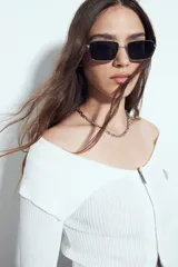 Top de punto acanalado negro, con diseño off-shoulder y escote amplio. Presenta mangas largas y cierre frontal completo con doble cursor, permitiendo ajustar la apertura superior e inferior.