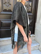 Ruana abierta de tejido de punto con acabado metalizado en color negro y dorado, con diseño de mangas amplias y terminación con flecos en el ruedo.