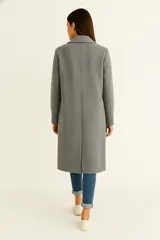 Tapado de corte recto y largo midi, confeccionado en tejido texturizado color gris. Presenta solapas clásicas, cierre frontal con botones y mangas largas.
