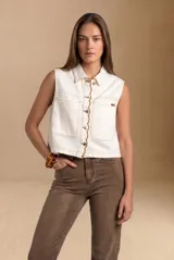 Chaleco de denim blanco sin mangas, con cuello camisero, bolsillos frontales plaqué con solapa y cierre frontal de botones con detalles de costuras onduladas en contraste.