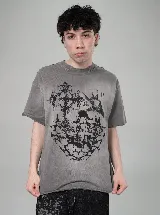 Remera de algodón de corte oversize, color gris con efecto lavado, con estampa frontal en serigrafía de estilo gótico que incluye una cruz y elementos abstractos.