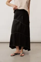 Falda larga de lino color beige, de corte asimétrico con costuras decorativas pespunteadas en contraste y diseño envolvente con bajo más largo en la parte trasera.