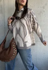 Sweater de punto con diseño abstracto de líneas orgánicas en tonos gris y beige, cuello redondo, manga larga con puños ajustados y corte holgado.