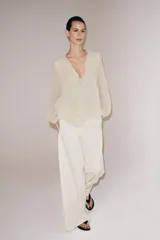 Blusa de viscosa color rosado con cuello redondo, manga larga abullonada con puños elásticos y cierre frontal con lazadas. Presenta un diseño con volantes en el bajo y corte asimétrico.
