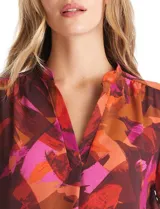 Blusa de gasa con estampado abstracto en tonos marrones, naranjas y fucsias. Presenta cuello mao con escote en V y mangas largas con sistema de ajuste mediante presilla y botón.