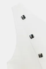 Top blanco de punto, escote asimétrico de un solo hombro, con detalle de botones metálicos decorativos en la parte delantera. El bajo es evasé con una abertura frontal central.