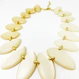 Collar corto con eslabones dorados y piezas de resina color marfil con forma de hojas. Cierre con mosquetón y largo regulable.
