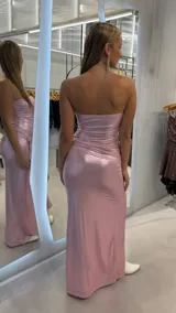 Vestido largo strapless de tejido metalizado en color rosado, con diseño ajustado, tajo lateral pronunciado y detalle fruncido con argolla dorada en la cadera.