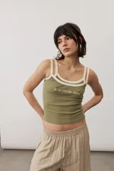 Musculosa de tejido rib color beige con detalles en marrón oscuro en el escote y doble tirante fino. Presenta un pequeño texto estampado en el pecho.