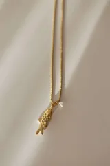 Collar de acero quirúrgico dorado con dije en forma de pez y detalle de perla colgante.