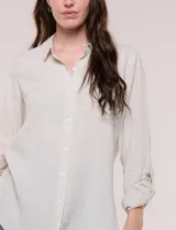 Camisa de lino marca Dash, color beige, con cuello con solapa, escote en V y cierre frontal con botones. Presenta mangas largas regulables con presilla y botón, y un bolsillo aplicado en el pecho.