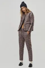 Chaqueta de jacquard color beige con estampado damasco en negro, corte boxy, vivos negros a contratono, amplios bolsillos frontales y botones a presión escondidos.