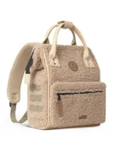 Mochila Cabaia modelo Adventurer Manchester, confeccionada en tejido tipo corderito color beige. Presenta asas superiores y detalles en cuero sintético color crema, bolsillo frontal con cierre y parche de la marca en el centro.