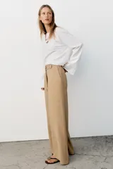 Pantalón recto color beige de tiro medio, con cintura elástica, bolsillos delanteros y cinturón ajustable con hebilla metálica dorada.