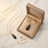 Collar de acero con baño de oro, compuesto por una cadena fina y un dije en forma de gota de piedra natural ónix negra con una circonia violeta engastada en el centro.