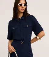 Camisa azul marino de tela airflow texturizada, con cuello clásico, mangas cortas con pliegues, cierre frontal abotonado y dos bolsillos de parche con solapa en el pecho.