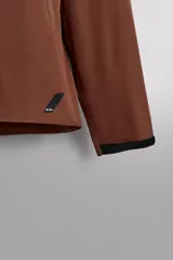 Cazadora deportiva color marrón confeccionada en tejido técnico de tres capas con membrana impermeable. Cuenta con cuello alto con capucha ajustable, mangas largas con puños reforzados ajustables, aberturas con cremallera en axilas, bolsillos frontales con cremallera y bajo ajustable con elásticos laterales.