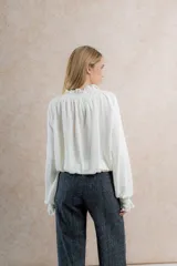 Blusa color crema de tela tejida 100% lana, con cuello fruncido y mangas largas con puños elásticos.