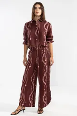 Pantalón de lino italiano color borgoña con estampado de cadenas en color rosa. De corte recto y talle medio, con cintura elástica en la parte posterior, bolsillos delanteros y aberturas laterales en el ruedo.